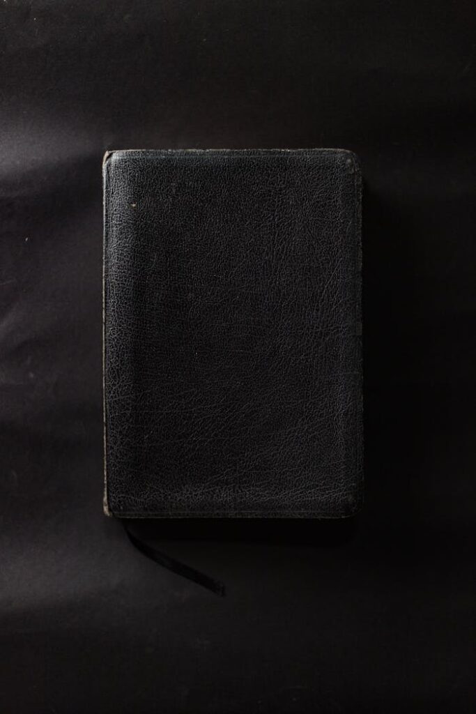 A closed black leather-bound book on a plain black surface.